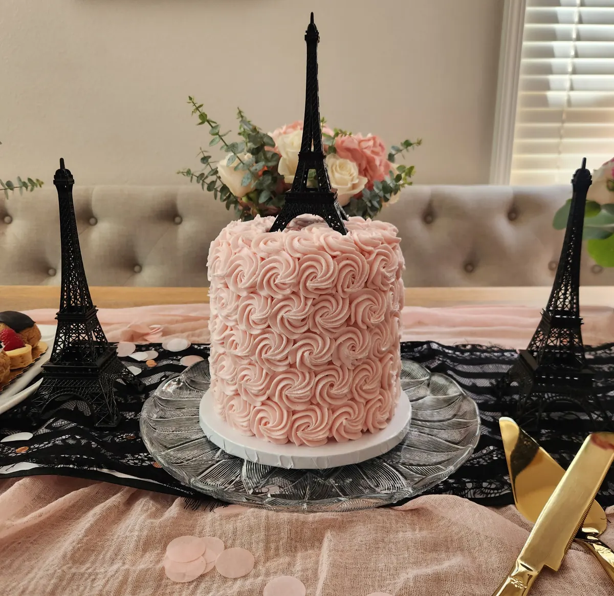 Pink rosette cake topped with a black Eiffel Tower, styled on a glass stand