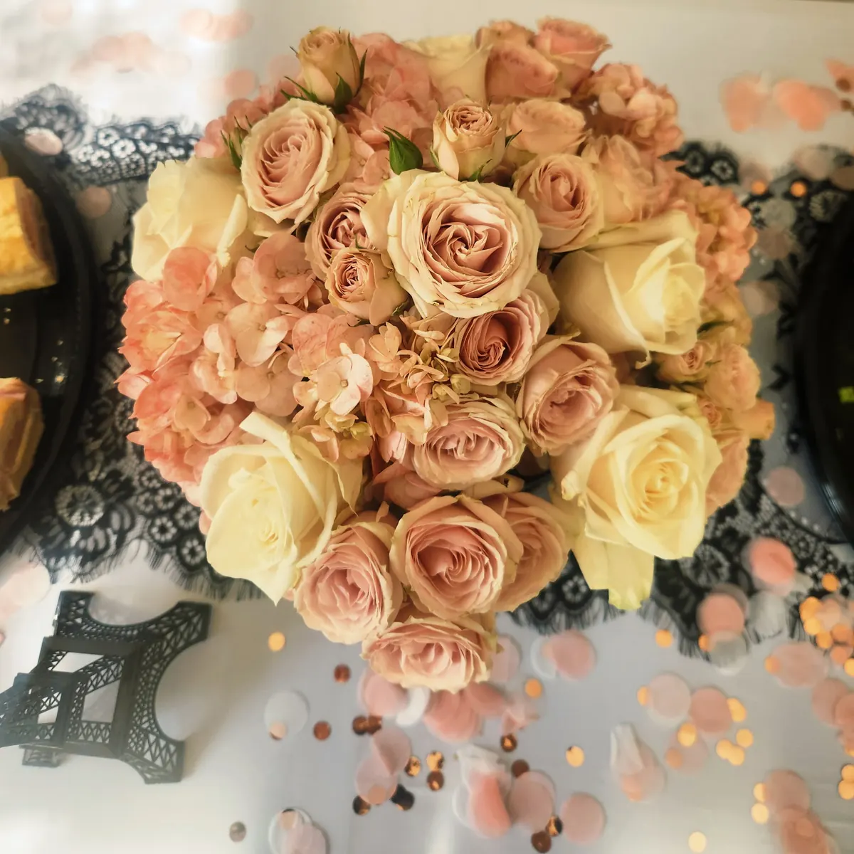 Overhead view of a blush, cream, and peach rose and hydrangea centerpiece on black lace