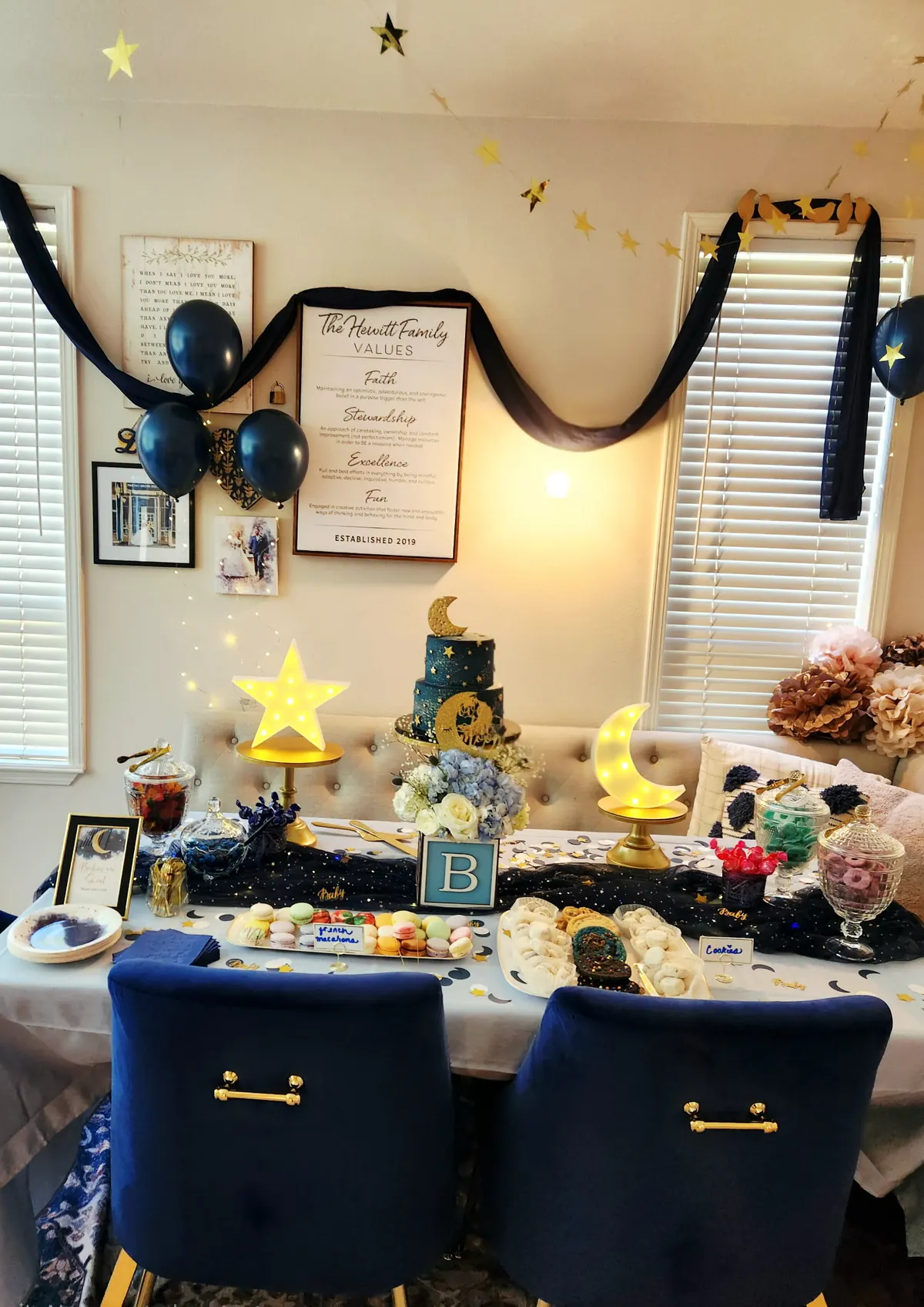 Dessert table in navy and gold with a tiered cake, macarons, and star garland