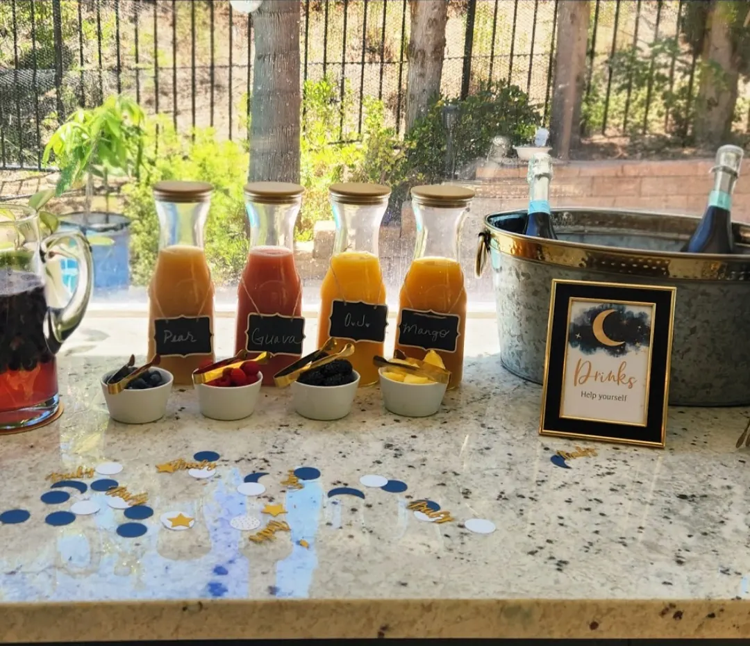 Drink station with labeled carafes of pear, guava, orange, and mango juice beside a moon-themed sign