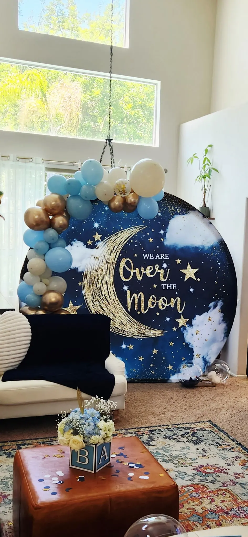 Circular Over the Moon backdrop with a gold crescent, stars, and a pastel balloon arch in a bright living room