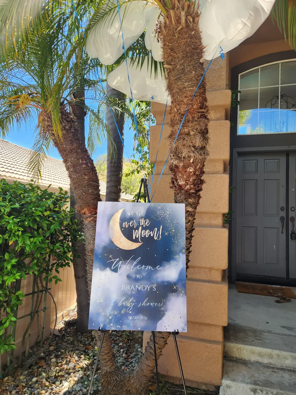 Welcome sign for an Over the Moon baby shower on an easel beside palm trees
